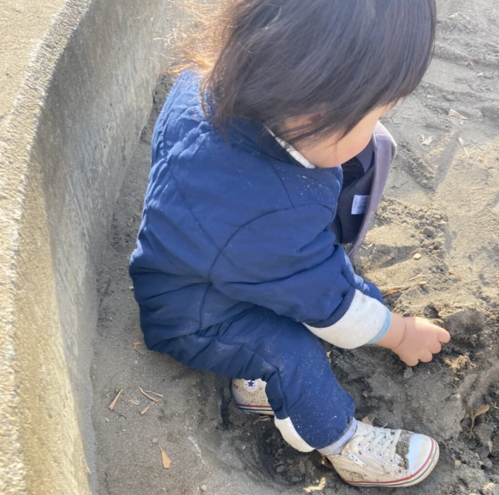 ジャンプスーツを着て砂場で遊ぶ赤ちゃん